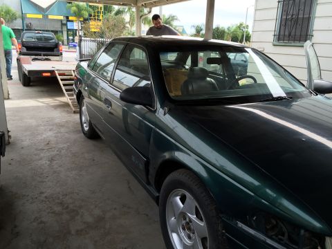 1993 Ford Taurus - A dark green sedan is parked under a covered area, with a pickup truck and trailer visible behind it.