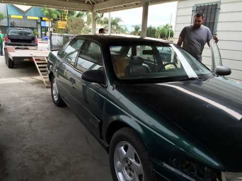 1993 Ford Taurus - A dark green 1993 Ford Taurus sedan is parked under a covered area, with a man standing by the open door.