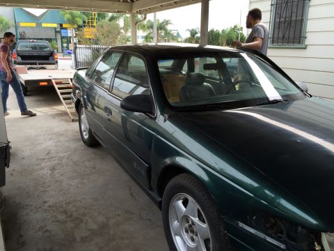 1993 Ford Taurus - A 1993 Ford Taurus is parked under a carport next to a pickup truck on a trailer.