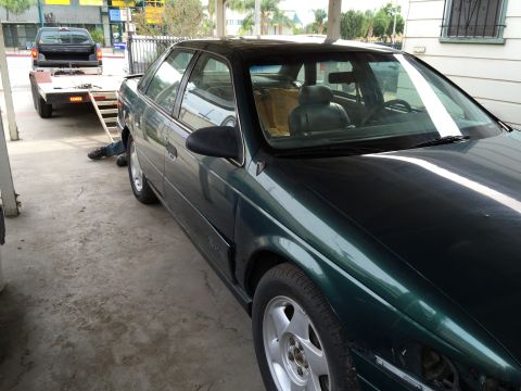1993 Ford Taurus - A dark green sedan is parked next to a trailer with a pickup truck being loaded.
