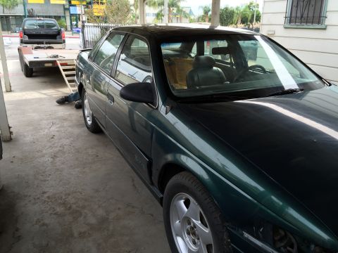1993 Ford Taurus - A dark green 1993 Ford Taurus is parked next to a trailer with a pickup truck on it.