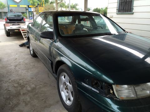 1993 Ford Taurus - A green sedan, possibly a 1990s model, is parked outdoors with a trailer and pickup truck nearby.