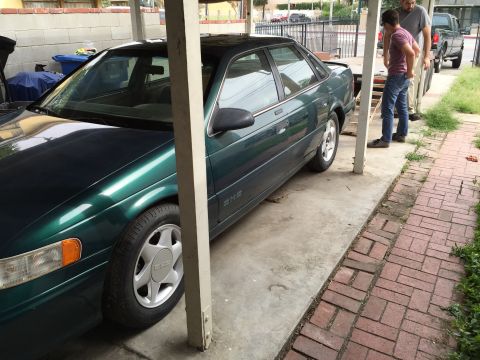 1993 Ford Taurus - A green sedan is parked in a carport with two men standing next to it.