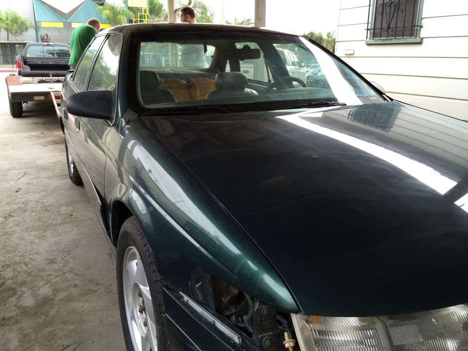 Dark green sedan with missing headlight, on a trailer