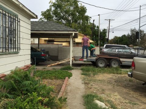 1993 Ford Taurus - Men loading lumber onto a trailer in a residential driveway with a green car nearby.