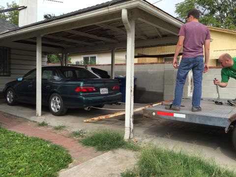 1993 Ford Taurus - A green sedan is being loaded onto a trailer, with two men present to assist the process.