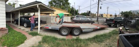 1993 Ford Taurus - A dark 1993 Ford Taurus sedan is parked under a carport next to a trailer being worked on.