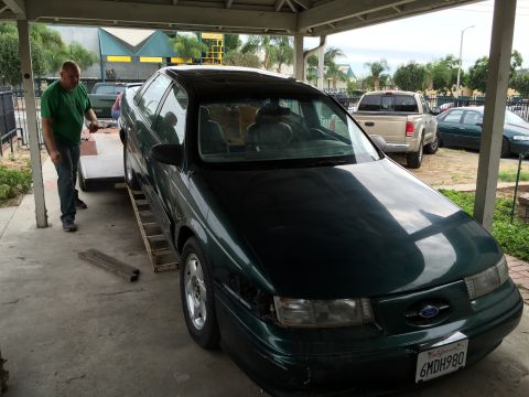 1993 Ford Taurus - A dark green sedan, likely a 1992 model, is being winched onto a trailer by a man in a green shirt.