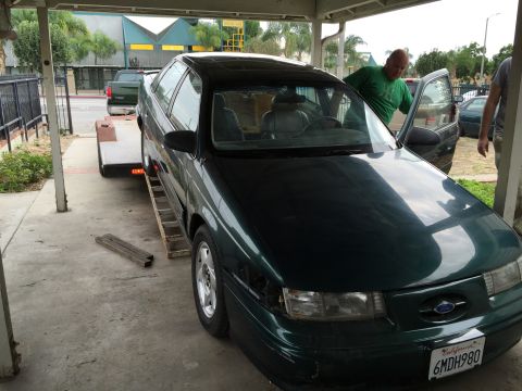 1993 Ford Taurus - A dark green sedan is being loaded onto a trailer, with a man opening the driver's door.