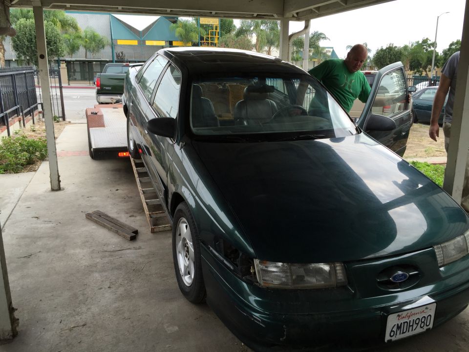 Dark green sedan on trailer, front quarter view. License plate reads 1990