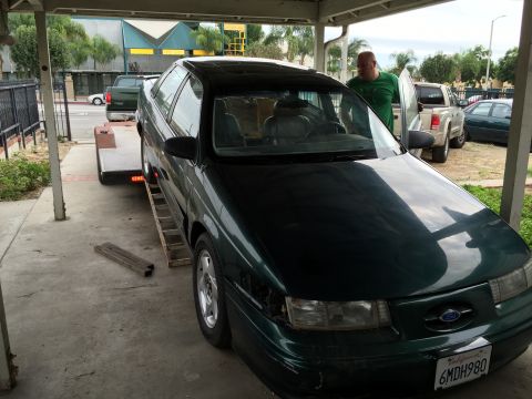 1993 Ford Taurus - A dark green sedan is being loaded onto a trailer, with a man standing next to the open driver's side door.