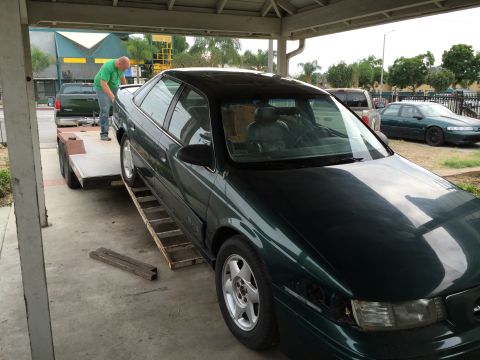 1993 Ford Taurus - A dark green 1993 Ford Taurus is being loaded onto a trailer, with another car visible in the background.