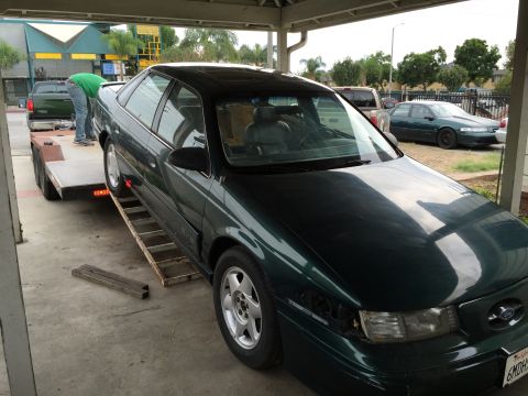 1993 Ford Taurus - A dark green sedan is being loaded onto a trailer, with another car visible in the background.