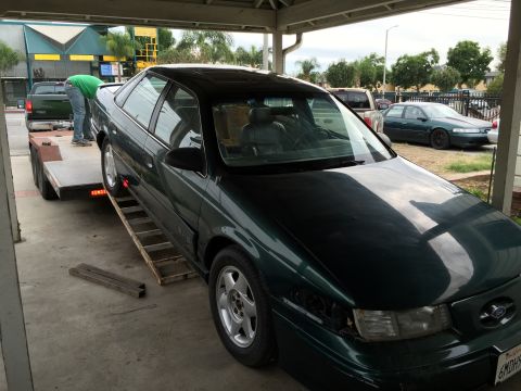 1993 Ford Taurus - A dark green sedan, likely a 1995 model, is being loaded onto a car trailer, with one headlight missing.