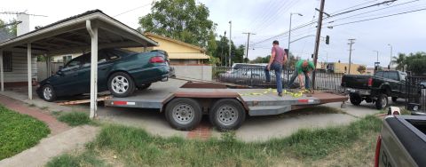 1993 Ford Taurus - A green sedan is loaded onto a car trailer, with a black pickup truck visible in the background.