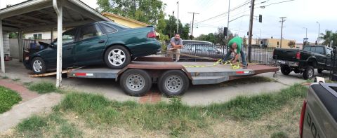 1993 Ford Taurus - Two men secure a green sedan onto a trailer, with a pickup truck visible in the background.