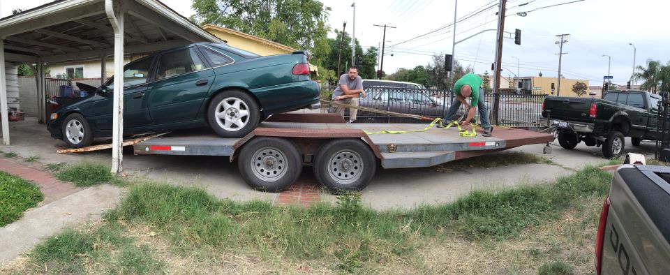Green sedan being loaded onto a trailer, with a pickup truck attached