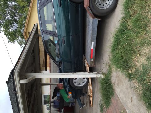 1993 Ford Taurus - A green 1993 Ford Taurus sedan is loaded onto a trailer under a carport.