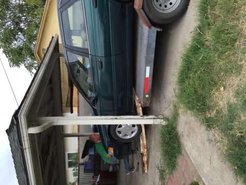 1993 Ford Taurus - A man is loading a green sedan onto a trailer in a residential driveway.