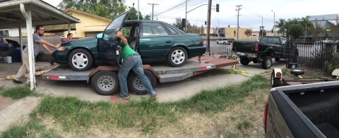 1993 Ford Taurus - Two men push a green sedan onto a trailer, while a black pickup truck is parked nearby.