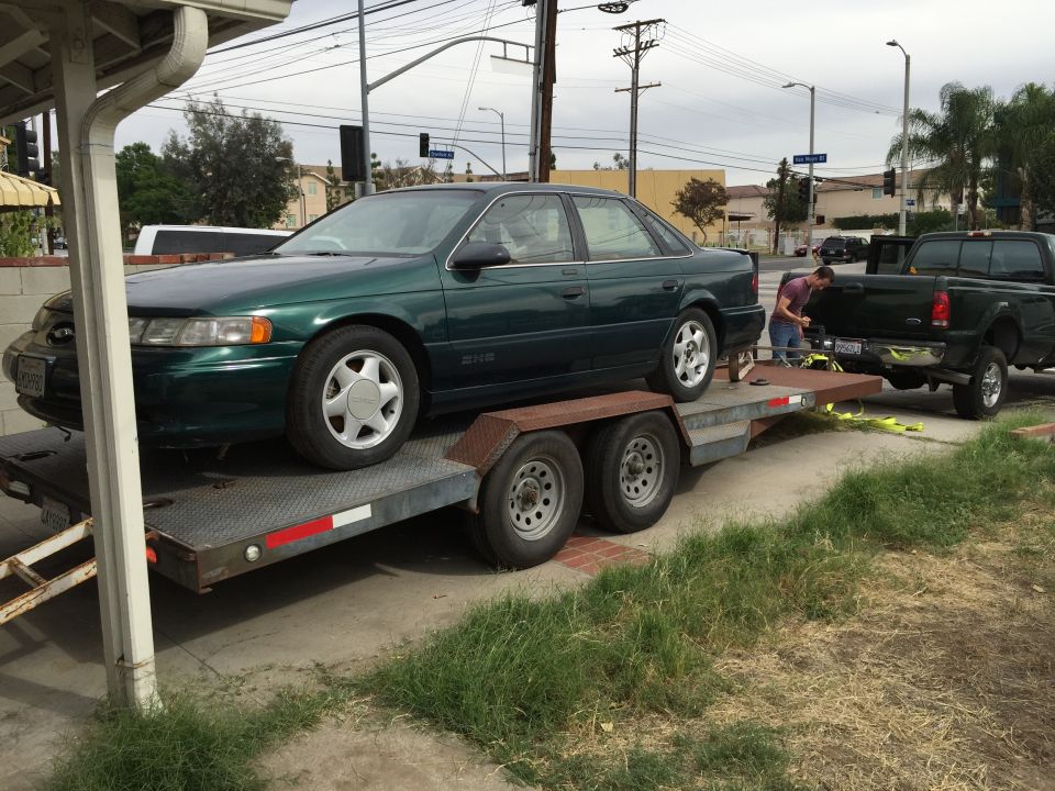 Green sedan on a trailer being towed by a pickup truck