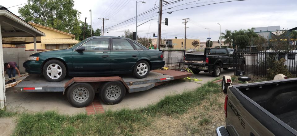 Green sedan on trailer, side view. Appears to be a 1995 Ford Taurus