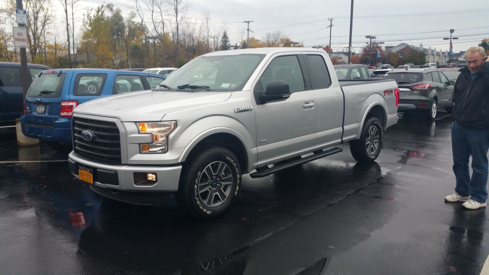 Silver 2015 Ford F-150 parked on a wet lot with a man standing nearby