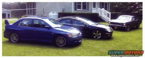 2006 Mitsubishi Evolution - Three cars, including a blue Mitsubishi Evolution, are parked on a grassy lawn in front of a house.