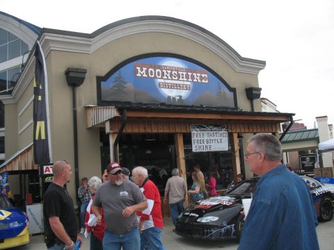 1972 Ford Ranchero - A scene outside the Moonshine Distillery with two race cars and several people gathered.