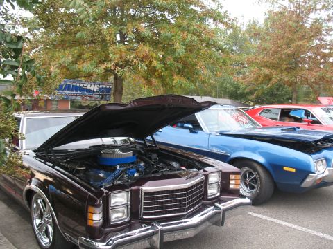 1972 Ford Ranchero - A lineup of classic cars, including a dark red vehicle with its hood raised, parked outdoors.