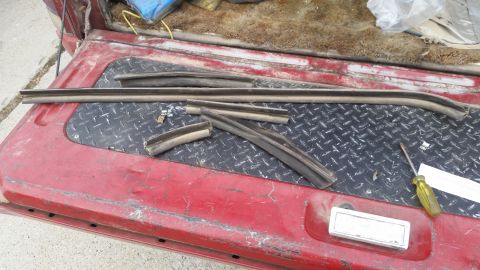 1981 Ford Bronco - Various weatherstripping pieces are laid out on the diamond plate of a red truck bed, alongside a screwdriver.