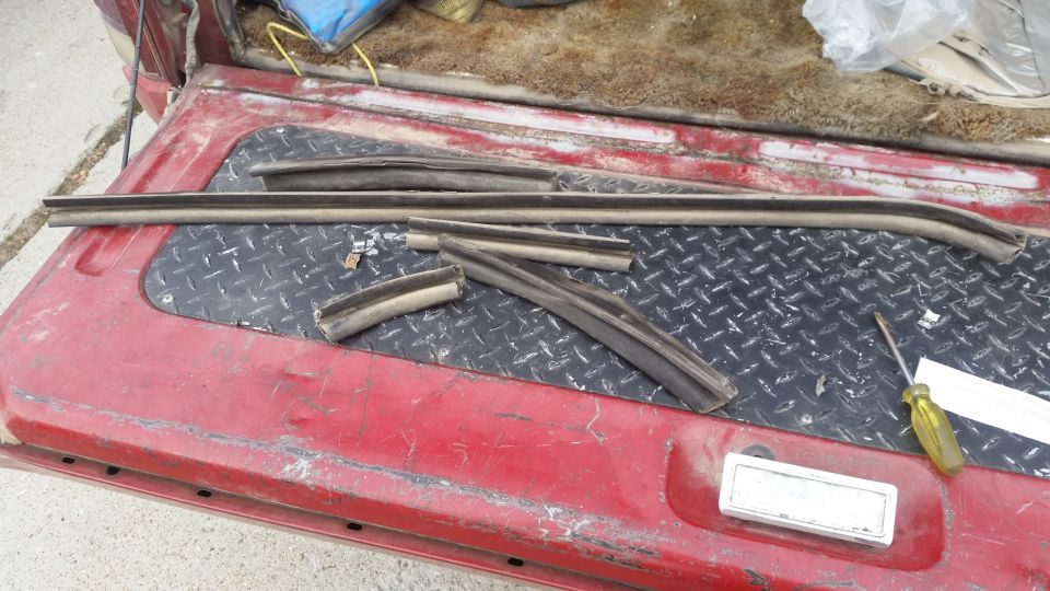 Weatherstripping parts on red truck bed with screwdriver