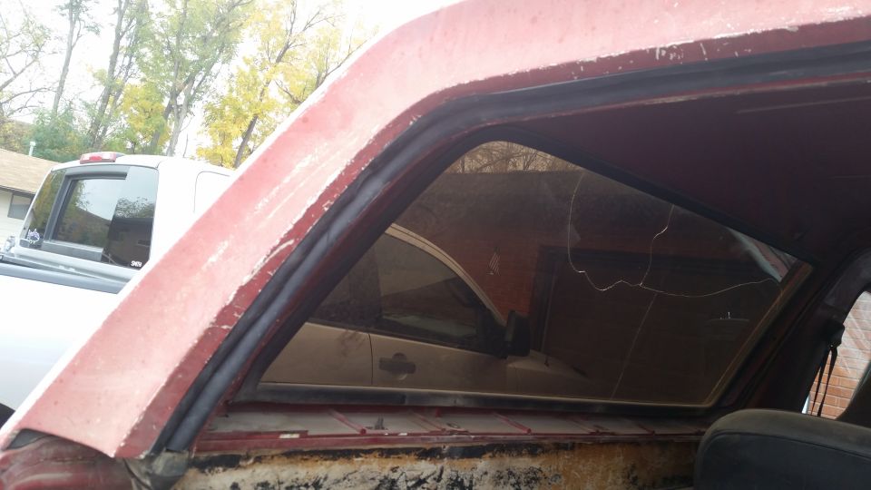Close-up of a red vehicle's interior showing a cracked window and weatherstripping. Another vehicle is visible through the window