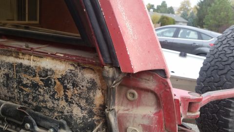 1981 Ford Bronco - Close-up of a red vehicle's door frame and weatherstripping, showing signs of wear and mud.