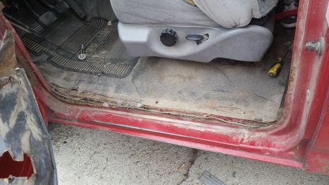 1981 Ford Bronco - The interior door sill of a 1981 Ford Bronco shows significant rust and damage, with a screwdriver visible on the floor mat.