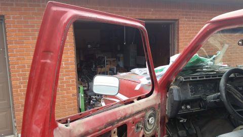 1981 Ford Bronco - The interior of a red truck is visible, with the driver's side door frame and dashboard in view.