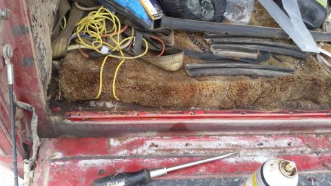 1981 Ford Bronco - The cargo area of a vehicle contains various items, including straps, rope, and weatherstripping, with a screwdriver visible on the floor.