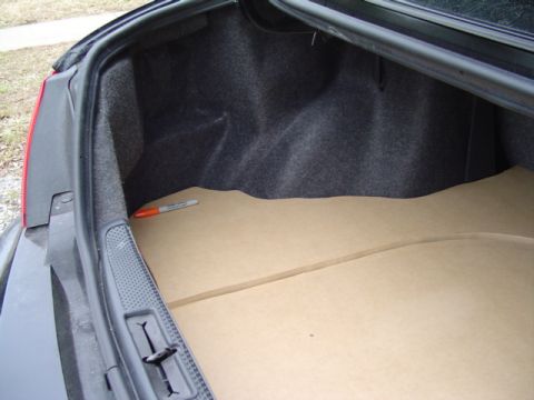 1999 Ford Taurus - Open sedan trunk with a two-piece MDF false floor template cut and fitted over the carpeted trunk pan, a marker left on the panel. Grey tru…