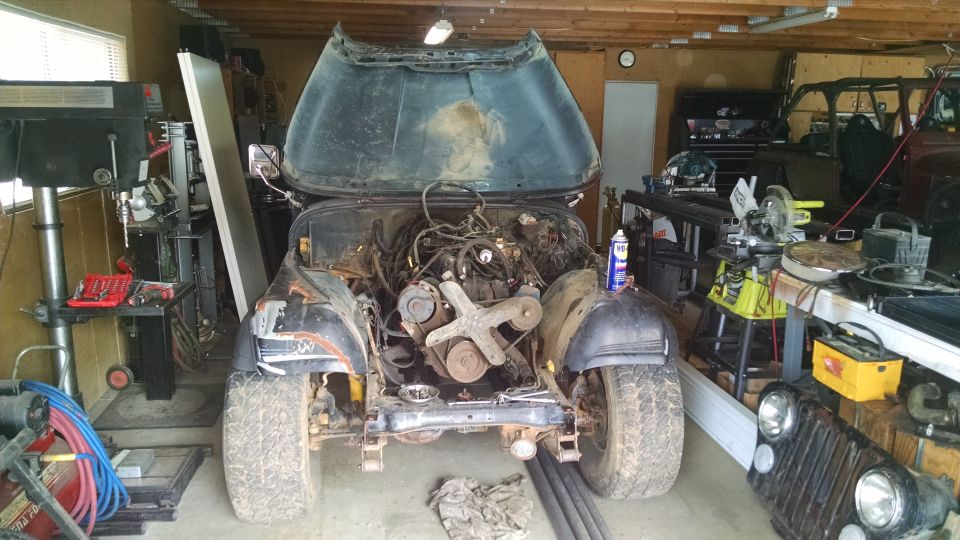 Jeep CJ in garage, hood open, engine out. Another Jeep front end visible to the right