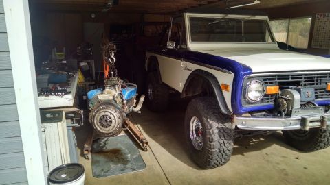 1985 Jeep CJ7 - A white and blue Ford Bronco is parked in a garage, with a detached engine on a stand nearby.