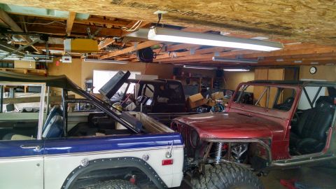 1985 Jeep CJ7 - Two off-road vehicles, a red Jeep and a blue and white SUV, are parked in a garage.