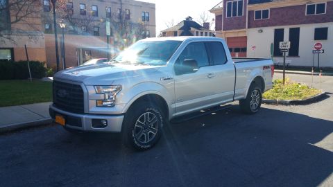 2015 Ford F-150 - Silver 2015 Ford F-150 SuperCrew pickup truck parked on asphalt in front of buildings.