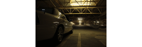 White sedan parked in a dimly lit garage, rear quarter view