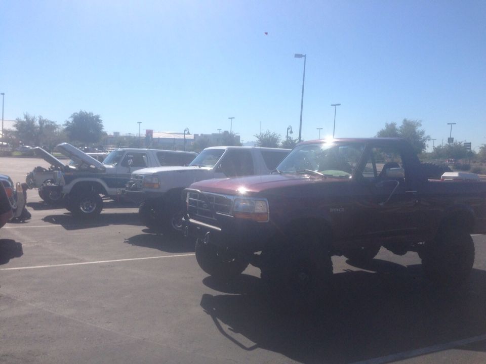 Maroon Bronco in front, white Bronco with hood up, and another white Bronco behind it in a parking lot