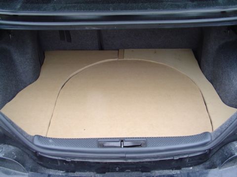 1999 Ford Taurus - Straight-on view into an open sedan trunk fully covered by a multi-piece MDF false floor, with a large curved cutout section outlined in th…