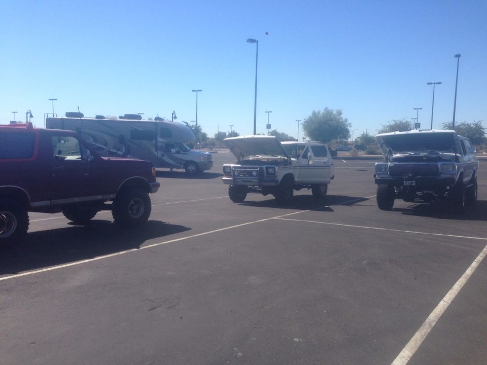 Three Ford Bronco SUVs parked in a lot, two with hoods up. One is maroon, the others are white and dark gray
