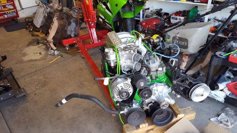 1988 Ford Bronco - An engine is displayed on a red engine stand in a garage, with a green motorcycle and various tools visible.