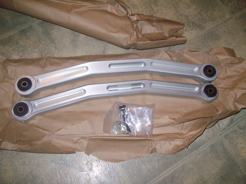 Pair of silver aftermarket control arms with hardware, laid on brown paper