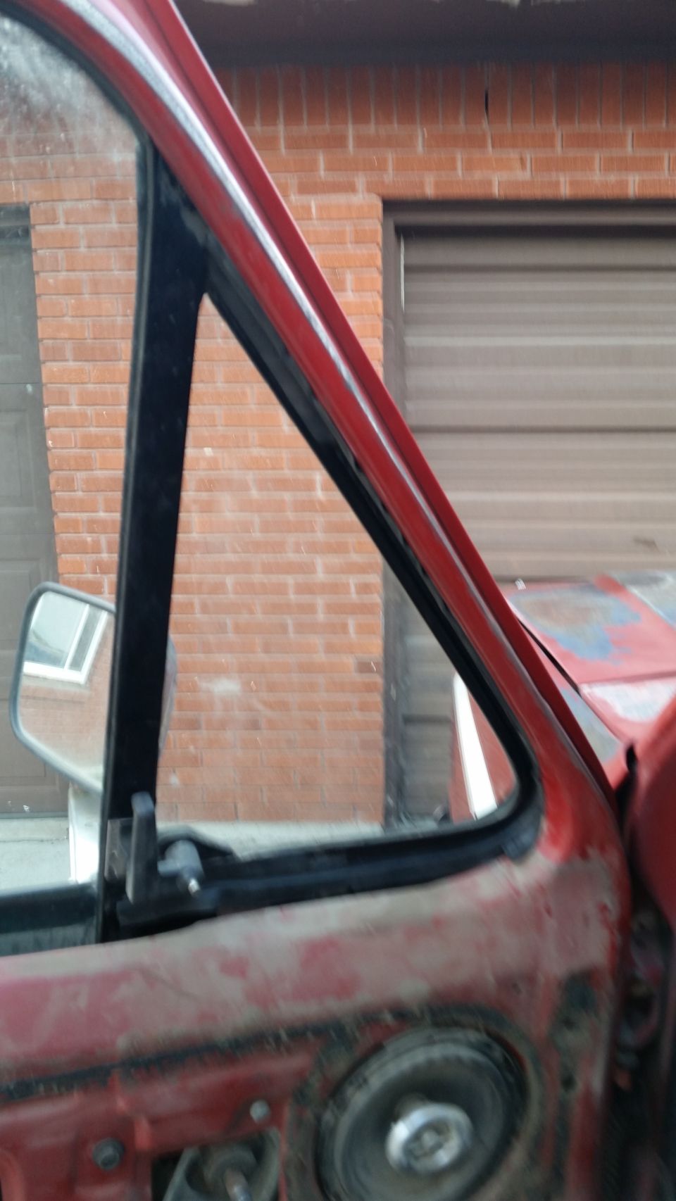 red truck door frame with side mirror, brick wall and garage door in background