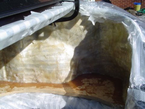 1999 Ford Taurus - First layer of fiberglass mat and resin laid over the rear bulkhead and quarter panel inside an open trunk, with amber resin puddled on the…